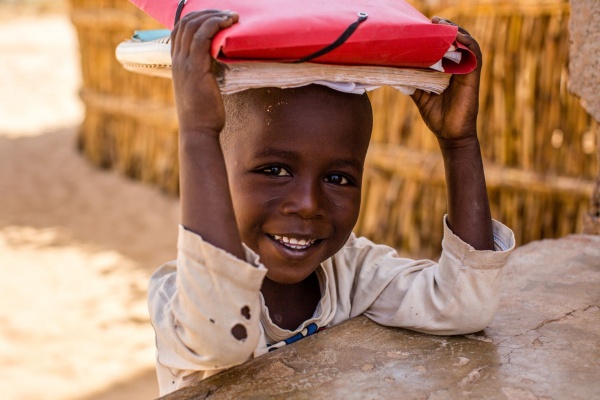 bambino africano sorridente sostiene sopra il capo dei libri di scuola