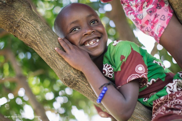 bambina sorridente appoggiata a ramo di albero 