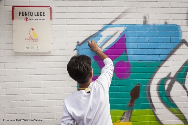 bambino al di fuori di un punto luce di save the children italia disegna un murales