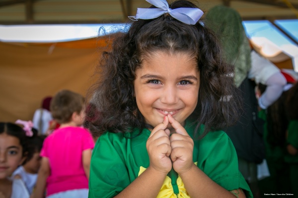 bambina con capelli castani vestita di verda e giallo tiene le mani davanti al viso mentre sorride