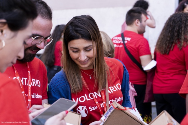 ragazza volontaria save the children insieme altri ragazzi volontari tutti con maglietta rossa dei volontari che leggono una brochure