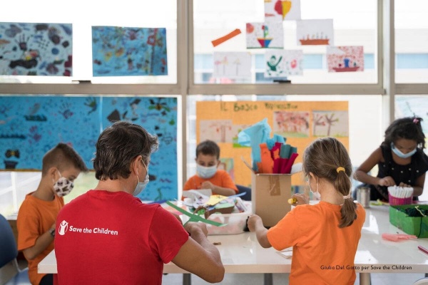 operatore di spalle con maglietta rossa e logo di save the children mentre insegna a quattro bambini nel Punto Luce di Roma