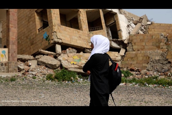 bambina in yemen con zaino in spalla di fronte ad un palazzo distrutto dalla guerra
