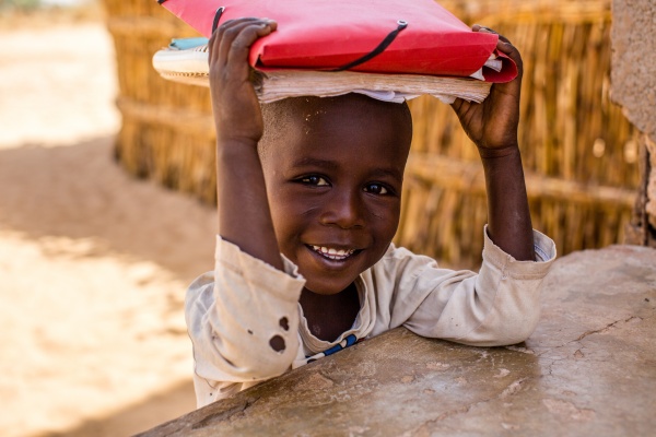 Regali Solidali Save the Children Bambino_africano_a_scuola_con_libri_sopra_la_testa_sorridente