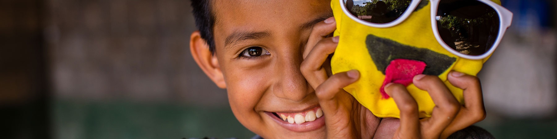 bambino sorridente in primo piano con una maschera gialla davanti a metà volto