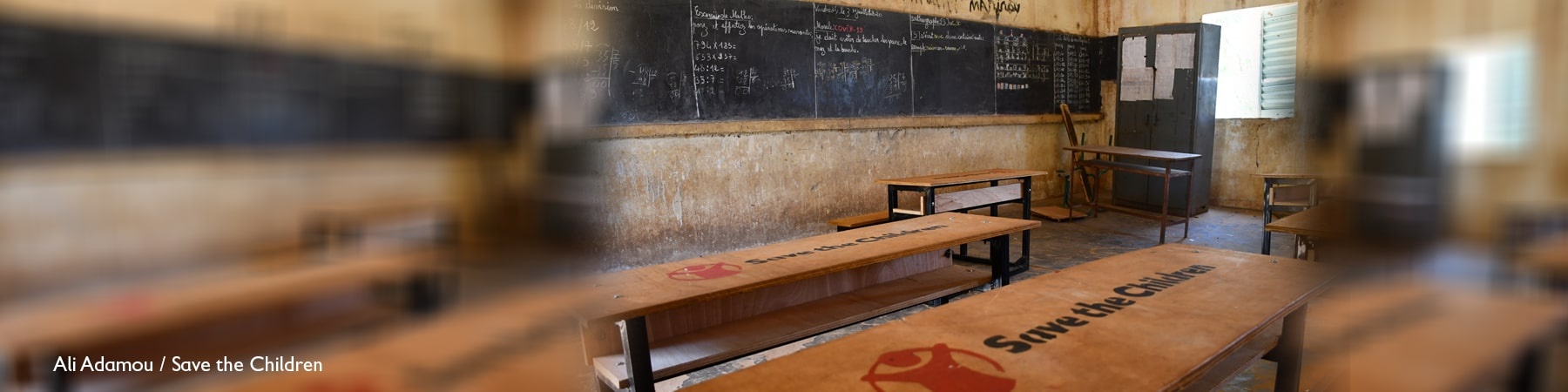 aula di scuola completamente vuota con banchi con logo save the children