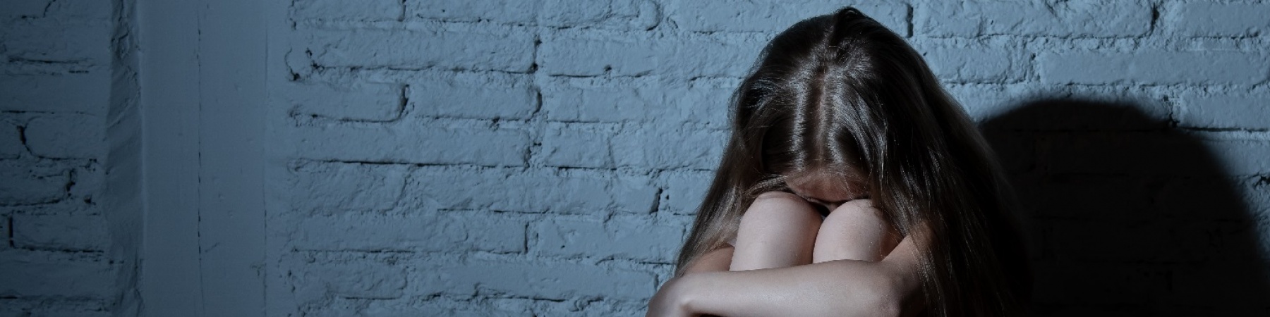 bambina rannicchiata davanti a un muro con la testa fra le braccia