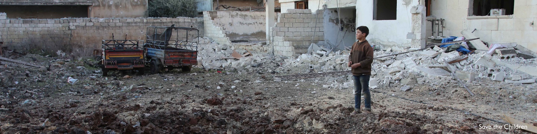 bambino in piedi in mezzo alle macerie provocate da un bombardamento in Siria ad Idlib