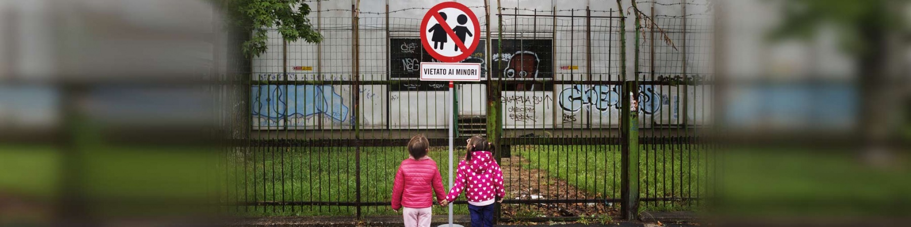 due bambine per mano davanti a un cartello con scritto vietato ai minori