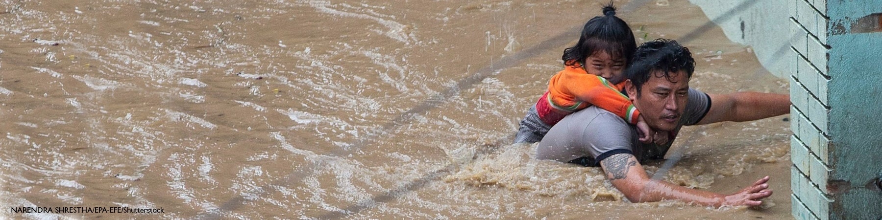 papà con la figlia sulle spalle cerca di uscire da un fiume creatosi dopo l inondazione