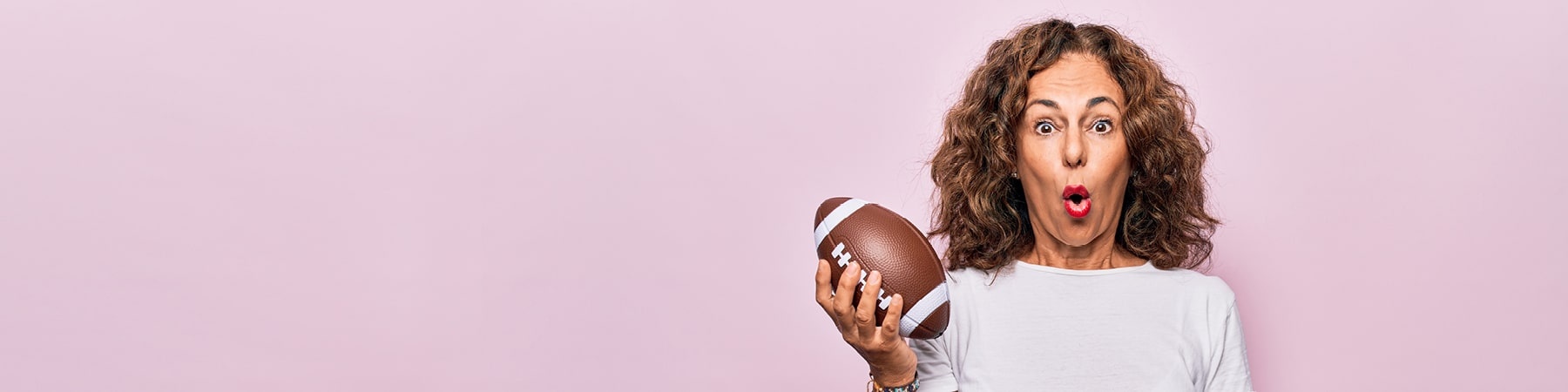 foto di una donna con in mano un pallone da rugby che guarda in camerina stupita, sfondo rosa
