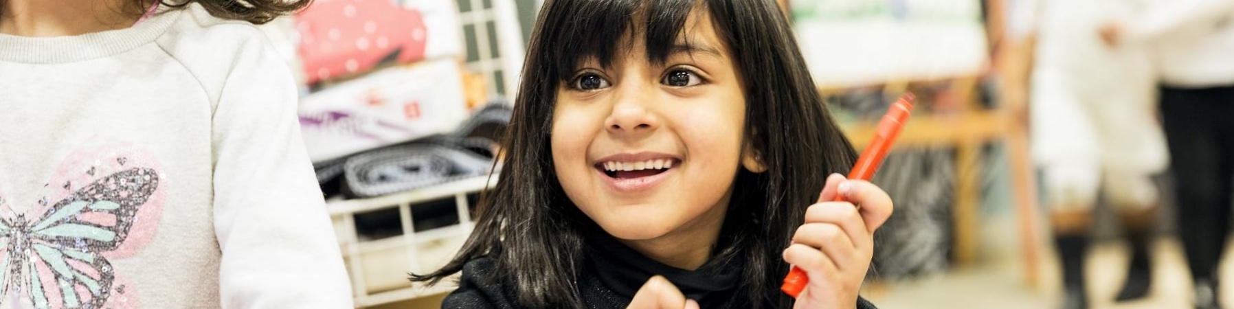 due bambine sorridenti in primo piano una ha in mano un pennarello