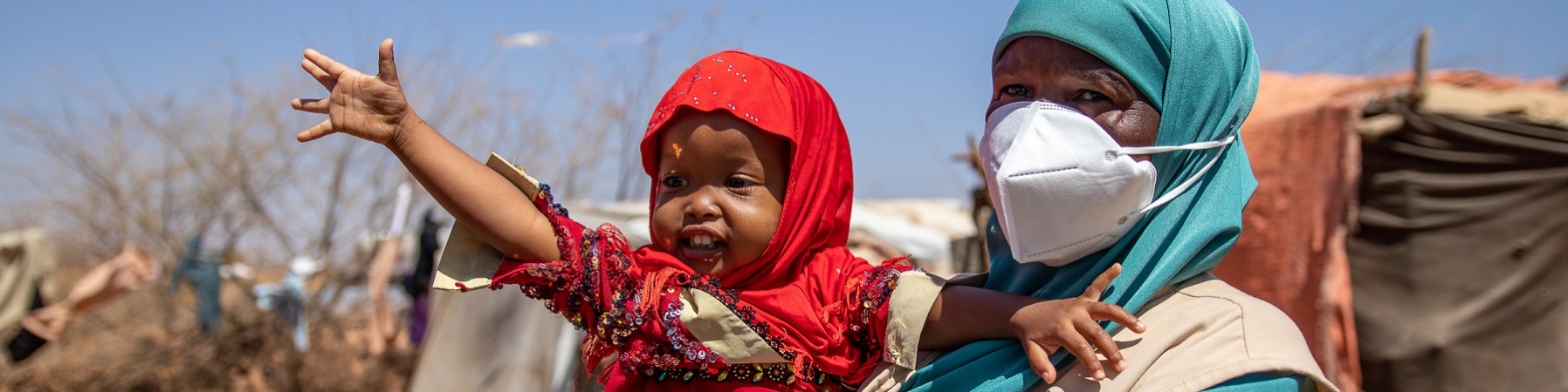 Bambina della Somalia vestita di rosso è in braccio a una operatrice save the children e ha il braccio alzato verso l alto