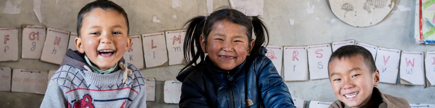 3 bambini asiatici sorridenti seduti a un banco di scuola