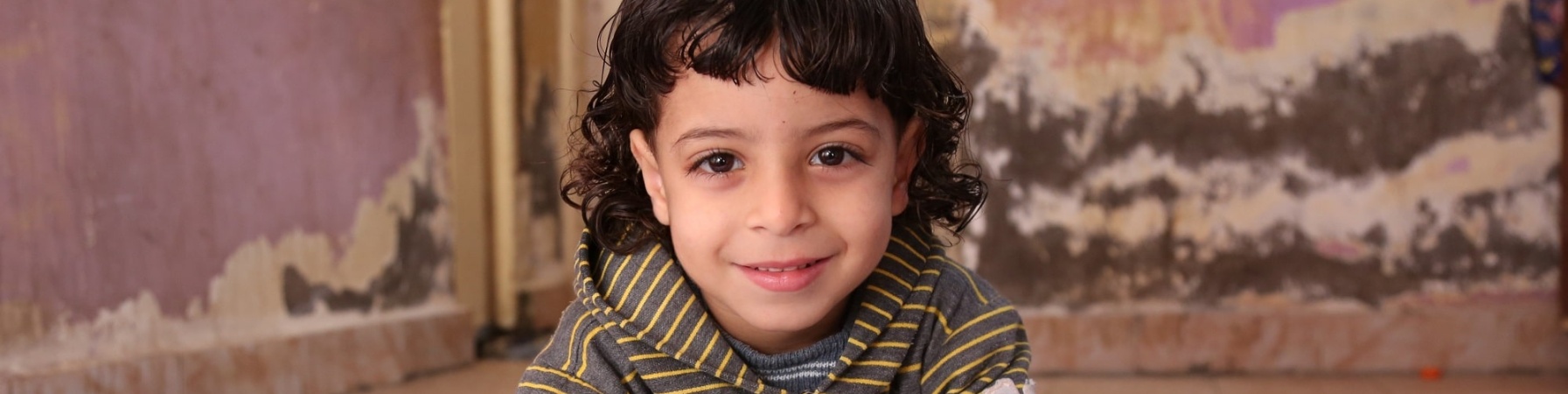 bimba egiziana con capelli neri a caschetto alla scrivania mentre disegna su un foglio bianco e guarda sorridente in camera