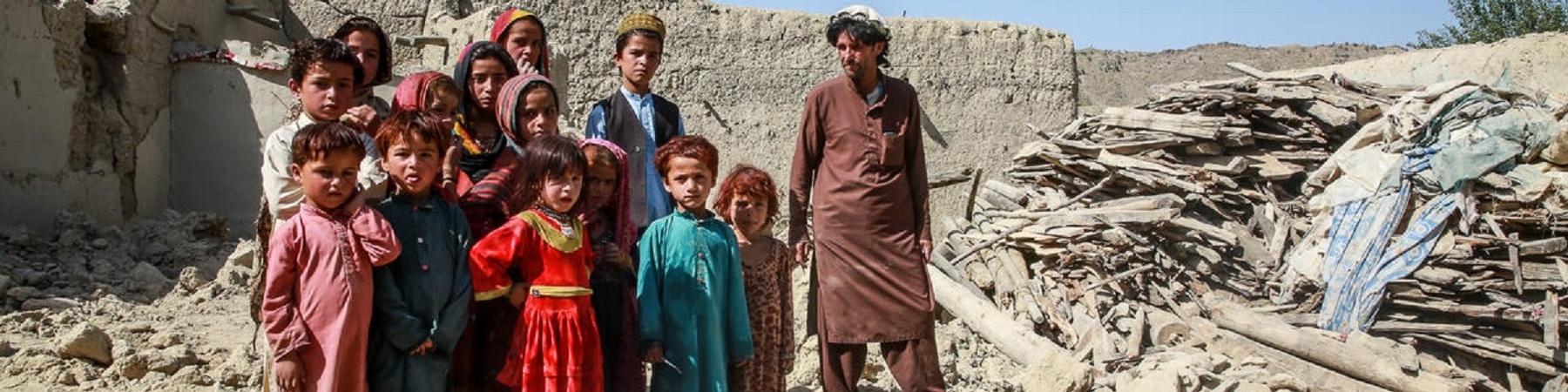 Bambine e bambini con accanto uno zio in mezzo ai detriti della loro casa distrutta dal terremoto in Afghanistan