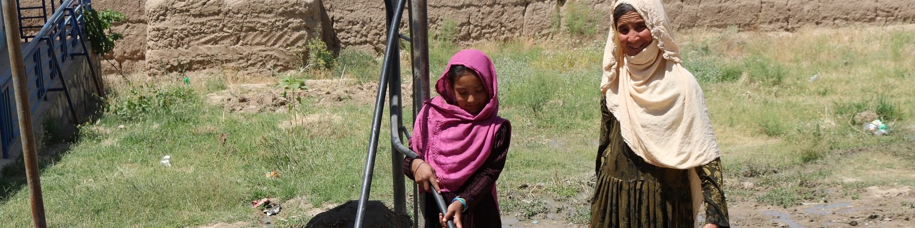 Due bambine afghane prendono acqua da una pompa in mezzo a un campo brullo
