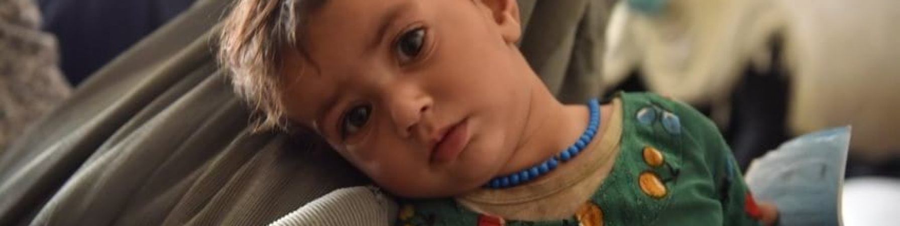 bambino afghano di due anni con camicia verde guarda in camera