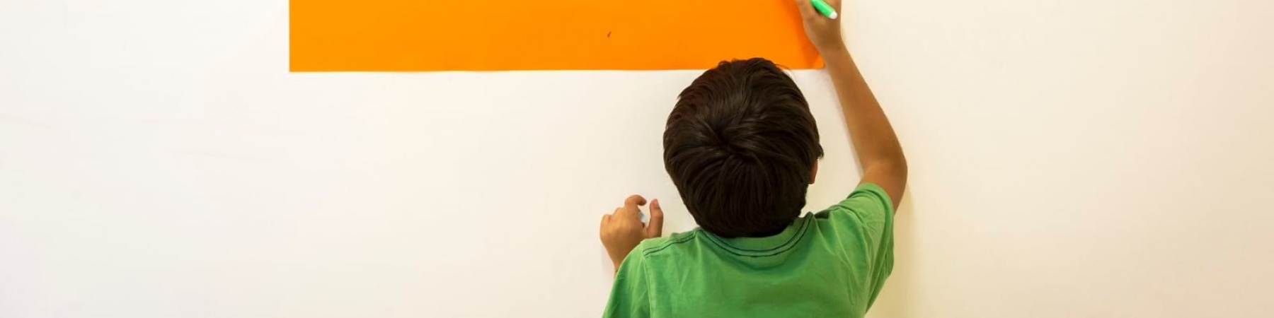 Bambino di spalle con maglietta vede scrive su un cartello appeso al muro le parole arcipelago educativo