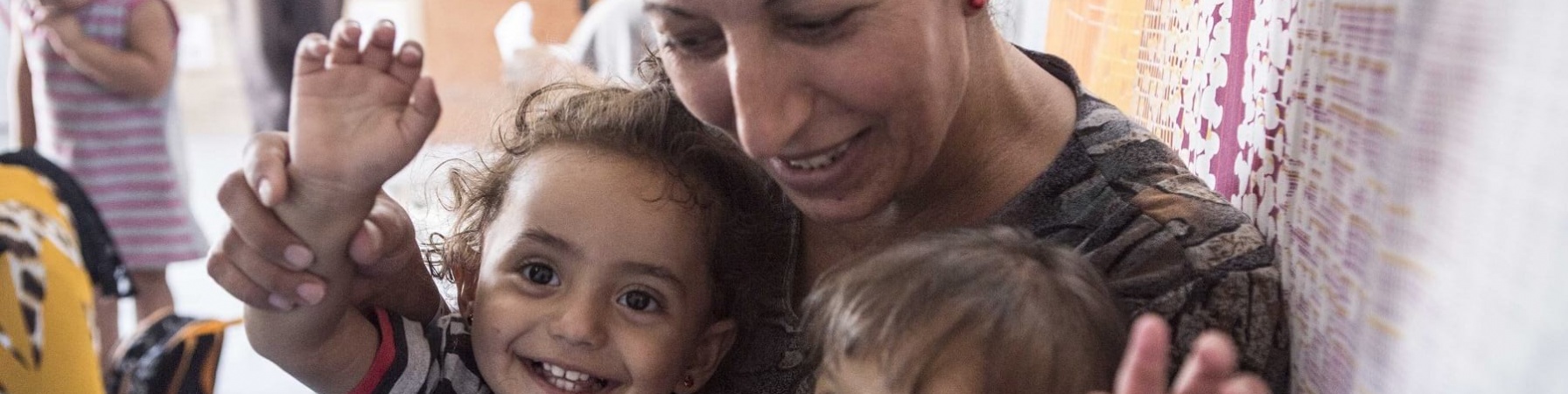 Una mamma abbraccia e guarda due bambini piccoli sorridenti