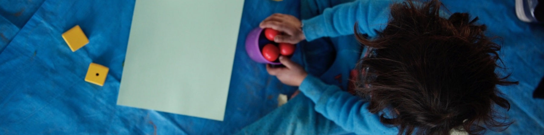 foto dall alto di bimba seduta per terra mentre gioca con delle palline rosse