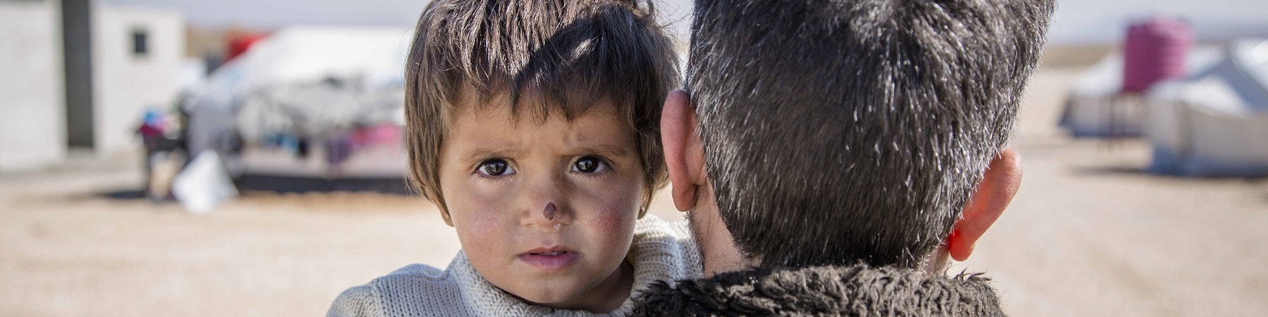 bambina siriana in braccio al papà di spalle