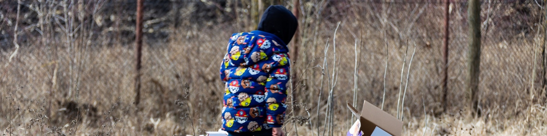 bambino con giacca blu che cammina tra alcune scatole e rifiuti sul ciglio di una strada