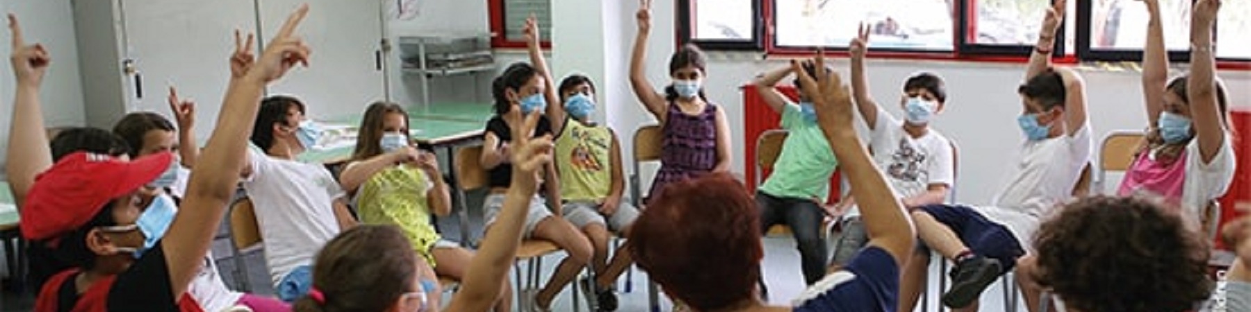 classe di bambini seduti in cerchio con le mani alzate