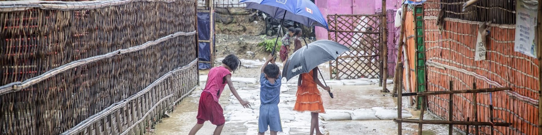 Tre bambini di spalle reggono ombrello e giocano in uno slum allagata del Bangladesh