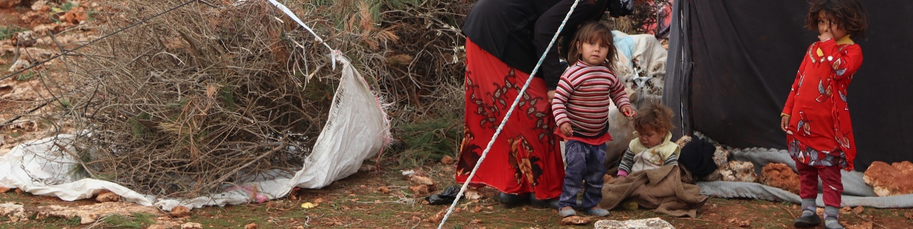 Tre bambini e una donna vicino alla tenda di un campo profughi.