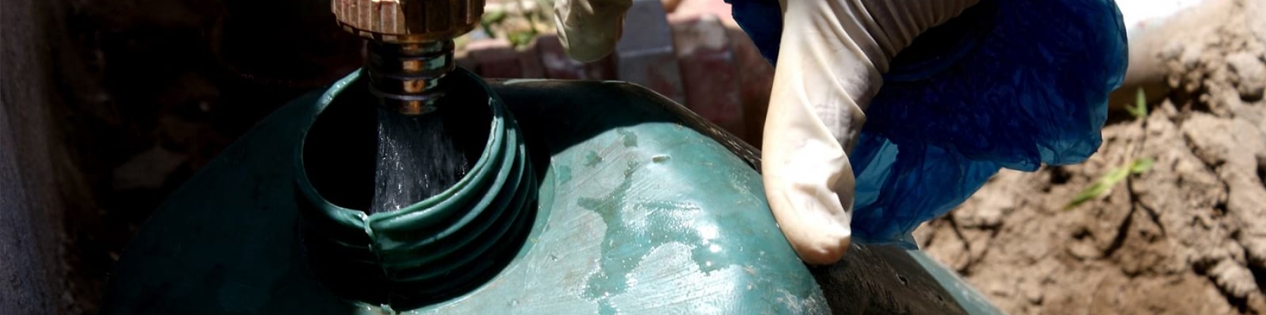 una mano con guanto in lattice apre rubinetto sopra tanica in plastica