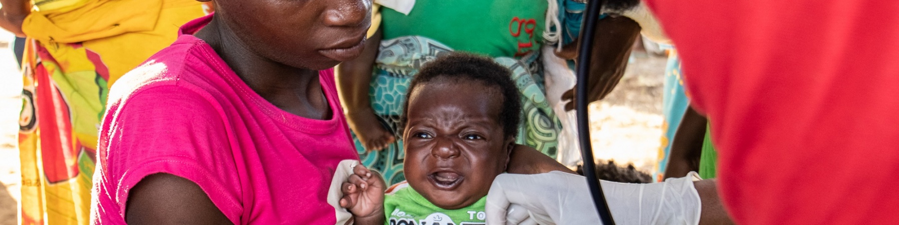 A sinistra operatore Save the Children visita un bambino tenuto in braccio dalla mamma. Siamo in Mozambico.