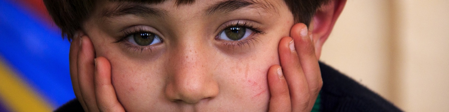 primo piano bambino imbronciato con la testa appoggiata tra le mani. Capelli a caschetto e maglioncino nero con righe bianche e verdi sui polsi.