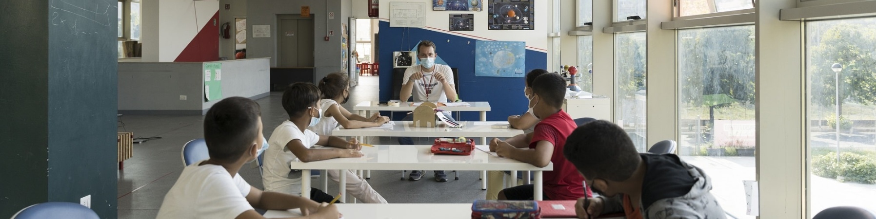 ragazzi e ragazze seduti ad un tavolo in un aula di un punto luce ascoltano un educatore che gli parla