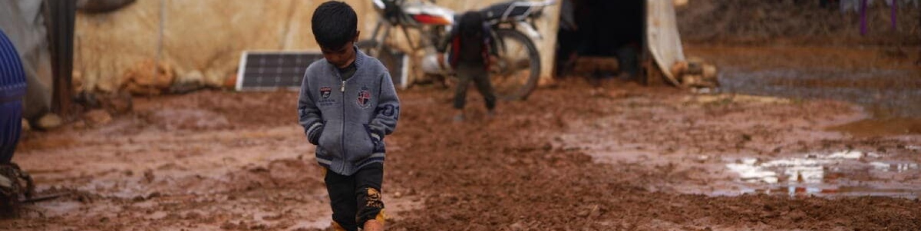 Bambino siriano deluso mentre cammina nel fango nel campo profughi