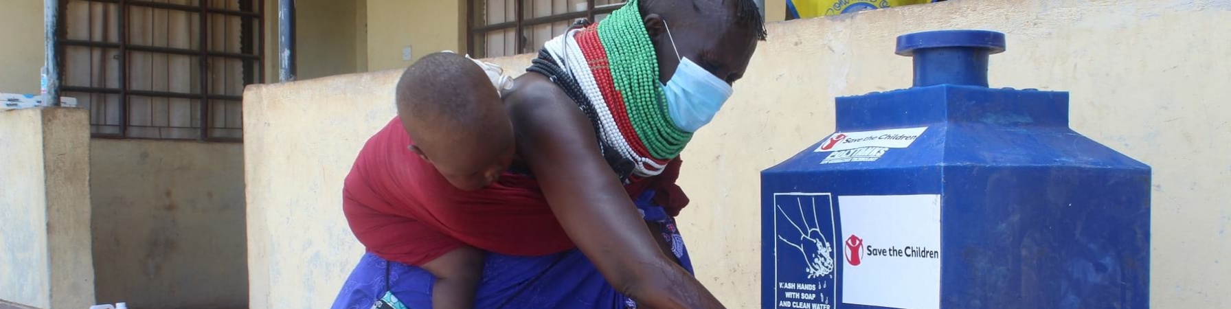 Mamma africana con bambino in fascia sulla schiena lava le mani con fontana mobile save the children.