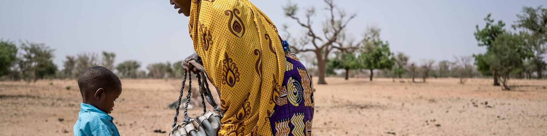 Campo lungo di madre e figlio nigeriani che si riforniscono di acqua in una terra brulla