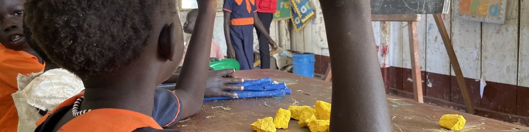 bambina ugandese di spalle con mano alzata durante lezione in classe