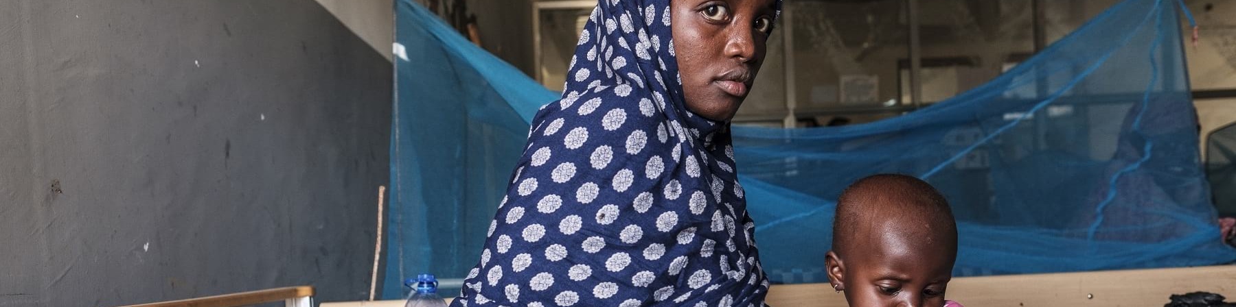 Mamma africana tiene in braccio bambino malnutrito entrambi sono seduto sul letto di una clinica