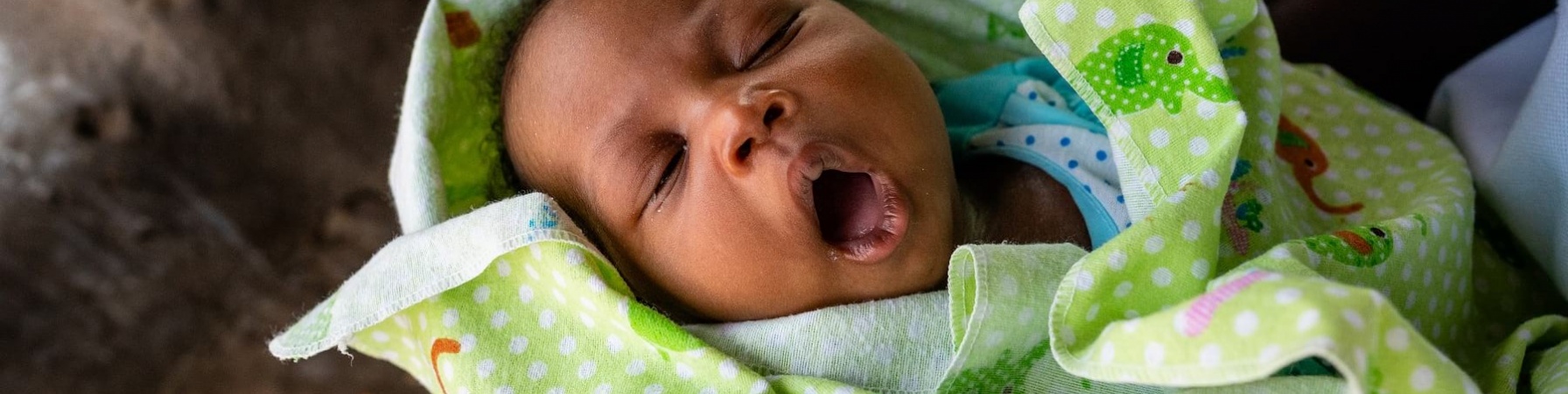 Primo piano neonato africano che sbadiglia avvolto in copertina verde