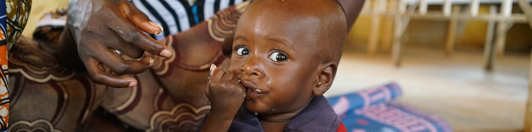 bambino nigeriano seduto a terra su un telo mangia plumpynut