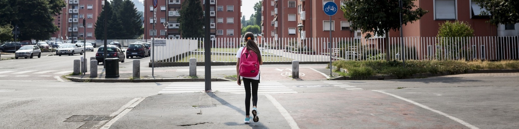 bambina di spalle cammina lungo una strada deserta a Milano tra i palazzi