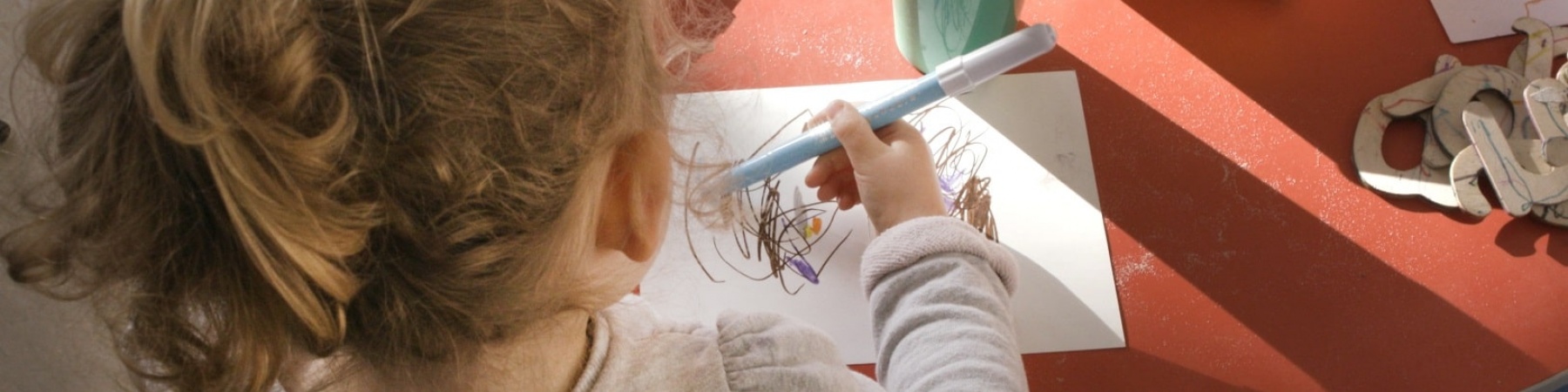 bambina di spalle alla scrivania che colora e disegna