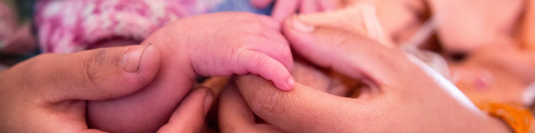 dettaglio delle mani di una mamma che tengono la mano del suo neonato