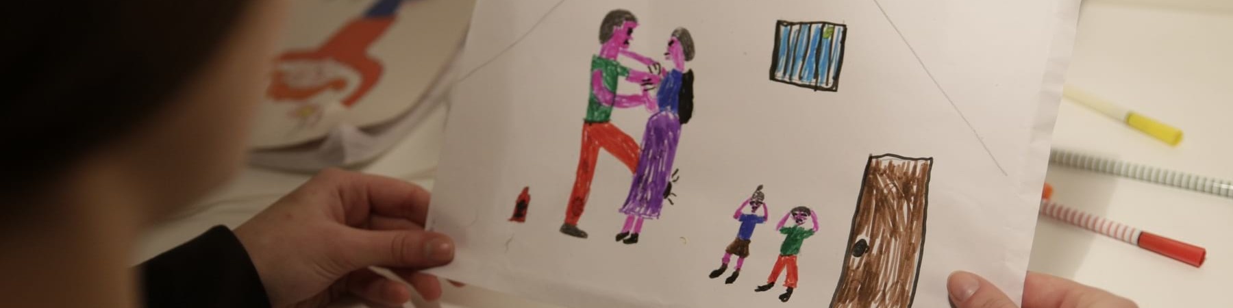 Bambina di spalle tiene in mano un disegno che rappresenta una scena di violenza domestica e assistita
