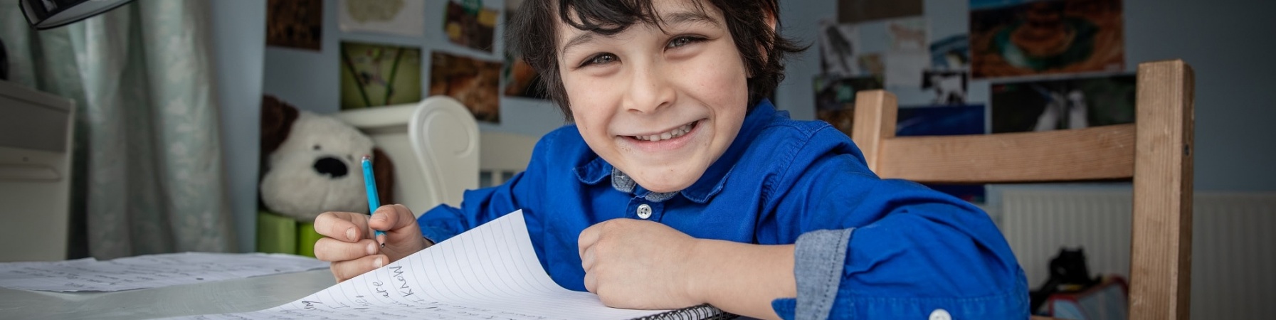 Bambino inglese seduto alla sua scrivania della camera mentre scrive su un quaderno