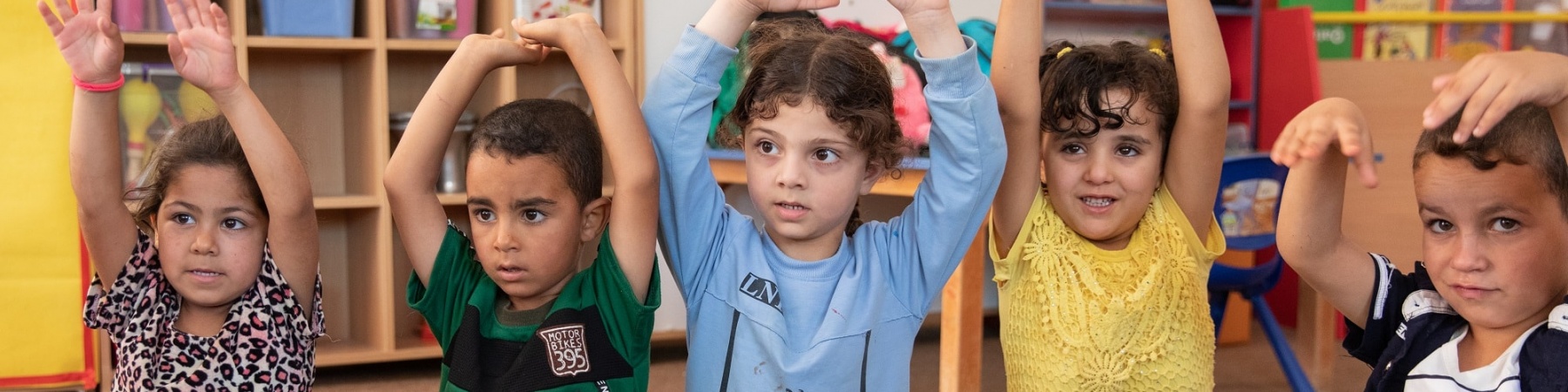 5 bambini seduti in cerchio con le mani alzate durante una lezione a scuola