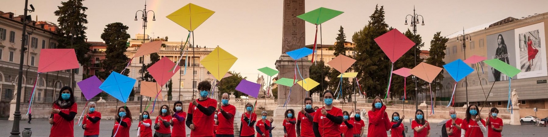 persone con maglietta rossa azione con aquiloni a roma davanti ad un arcobaleno