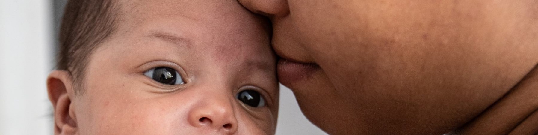primo piano di un neonato in braccio alla madre che gli bacia la fronte