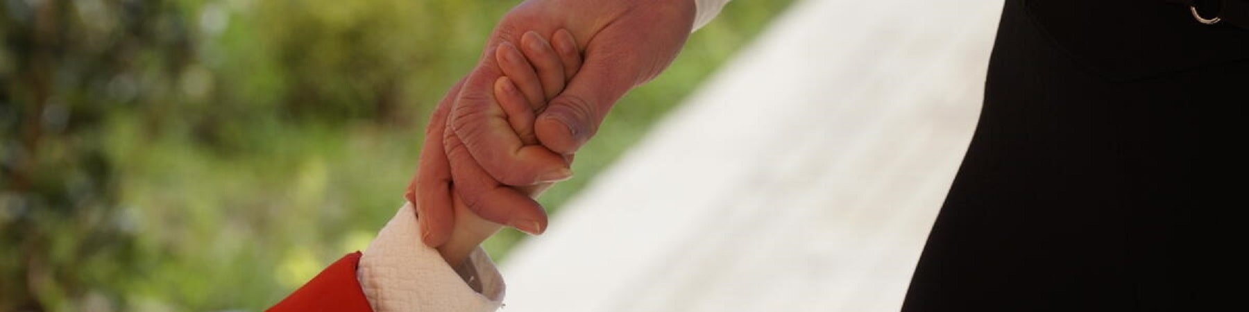 mano di un bambino con la magglietta rossa che si unisce alla mano della madre con maglietta nera su sfondo di un giardino